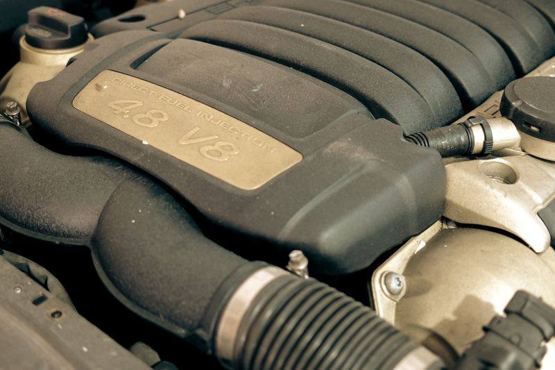 A Porsche Cayenne engine bay with the cover carrying its 4.8 V8 plaque, intake ducting alongside.