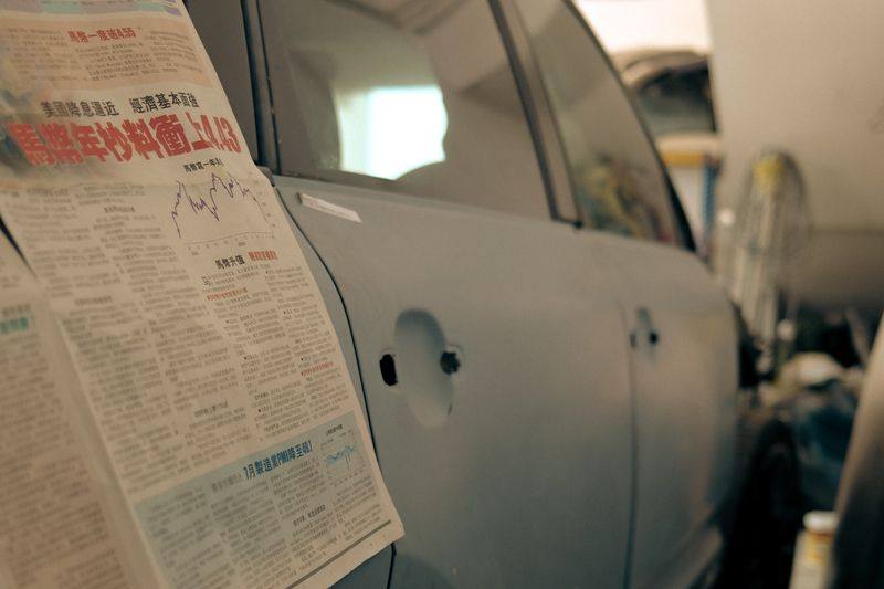 A vehicle in primer with its glass masked using sheets of newspaper.