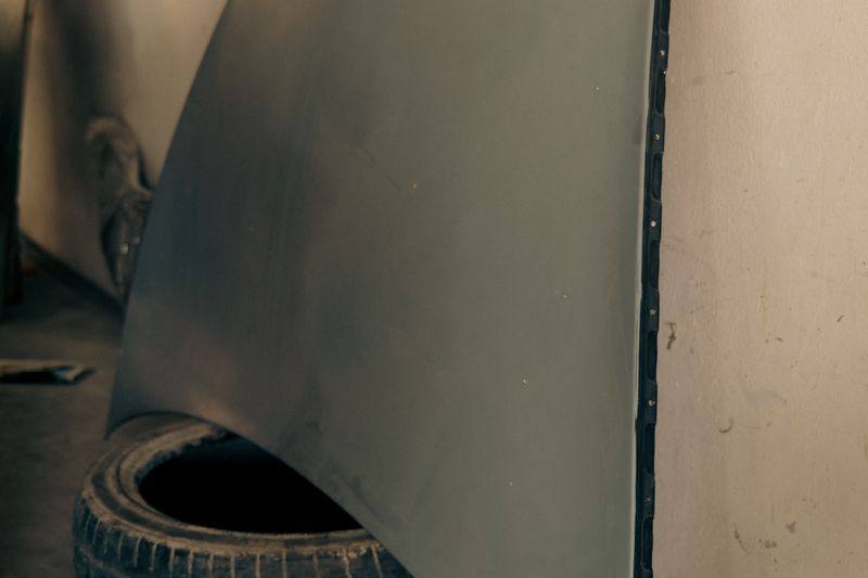 A bonnet in grey primer leaning against a workshop wall beside a tyre.