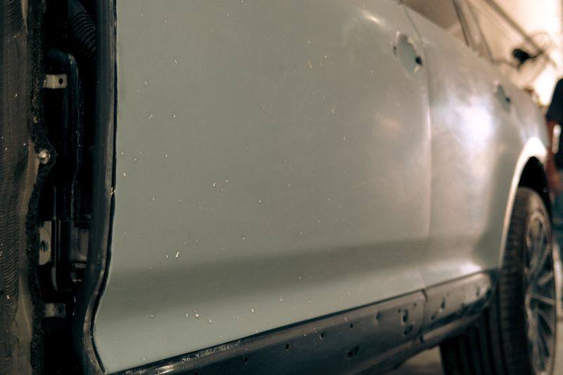 The side of a vehicle in grey primer, door and sill prepared, glass still fitted.