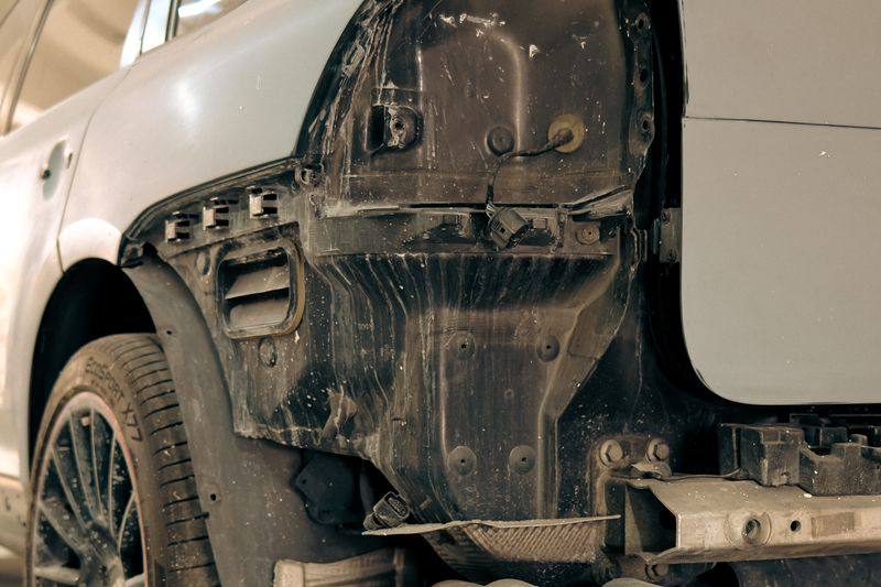 The rear of a stripped SUV in a workshop, bodywork removed, quad exhaust tips visible.