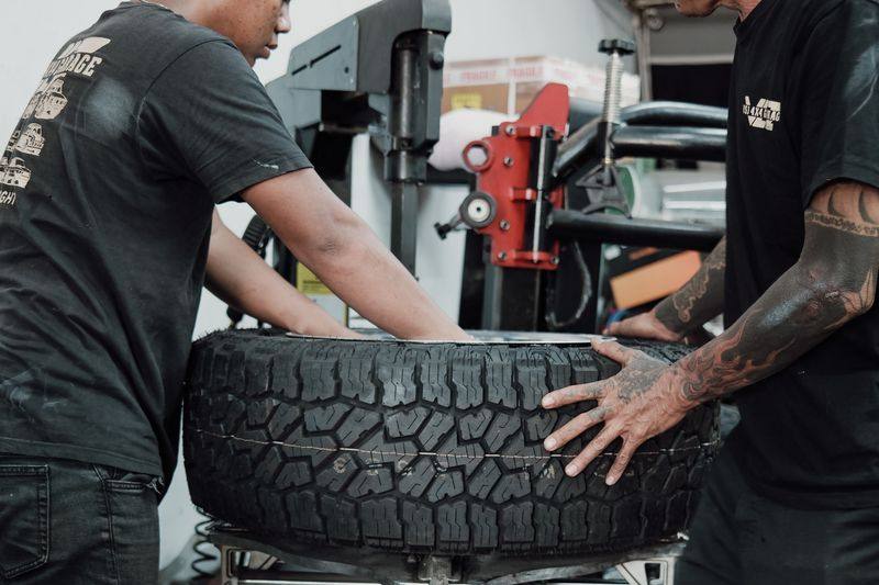Two people fitting a tyre to a wheel on a tyre machine in a workshop.