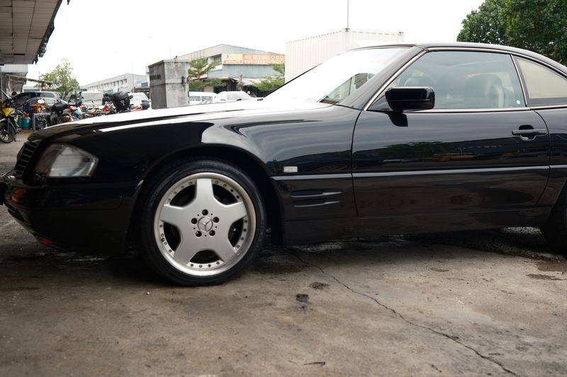 A black Mercedes-Benz R129 SL seen from the front three-quarter, from Project Kaiser.
