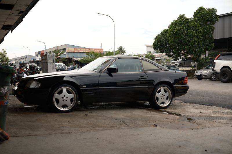 A black R129 SL seen from the side at a slight angle, parked outdoors.