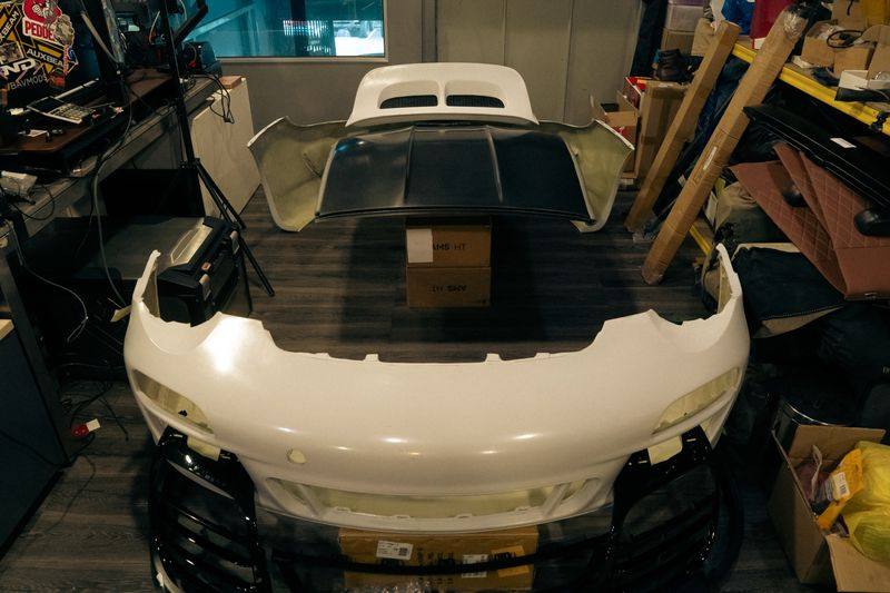 A white composite front bumper and a vented bonnet laid out on a wooden floor in a storeroom.