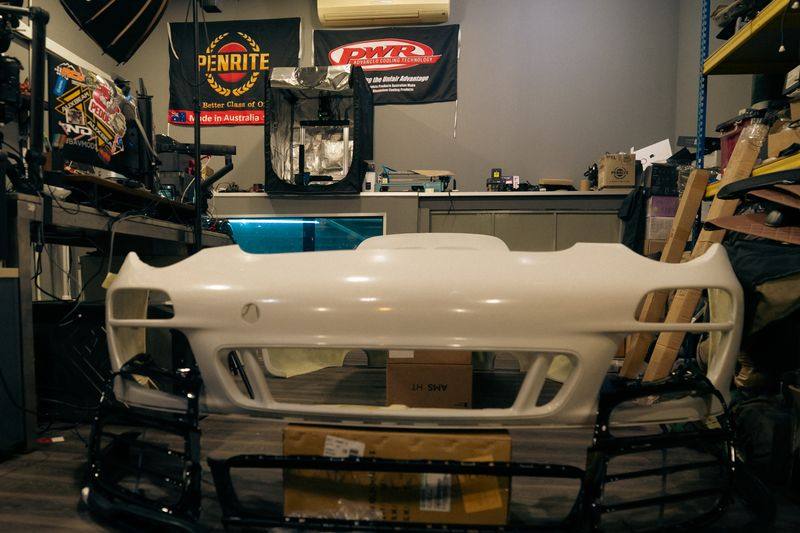 A white composite front bumper viewed head-on, with black lower sections in front of it.