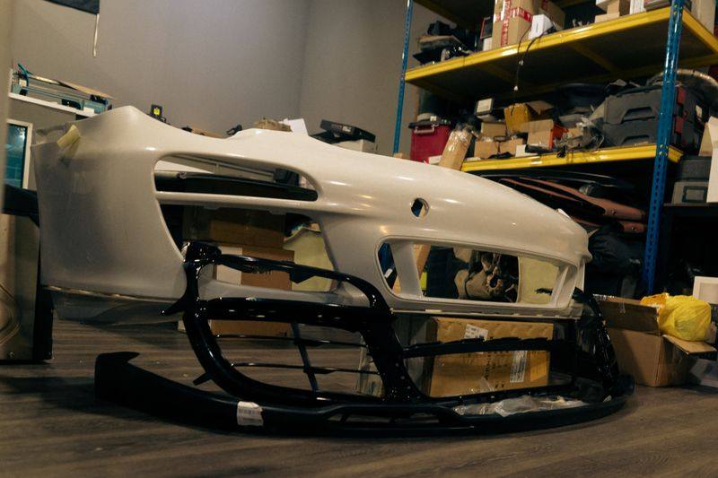 A front bumper with its black lower valance and grille sections laid out beneath it.