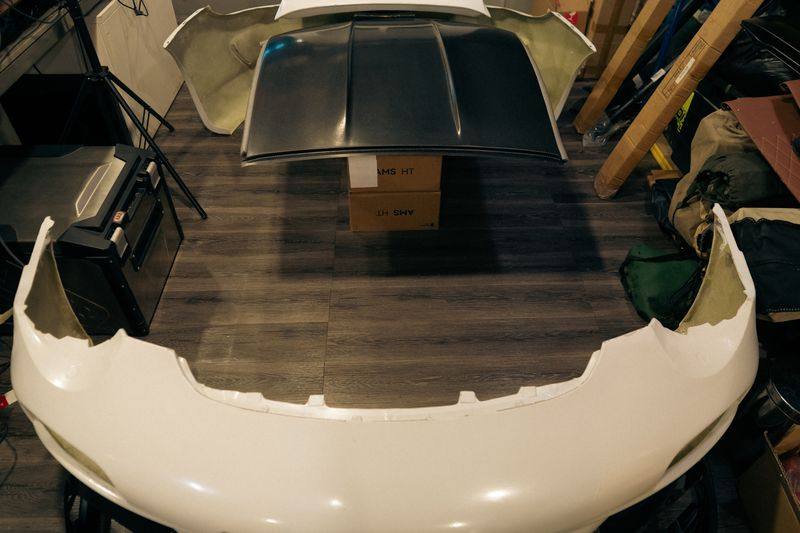 A front bumper and a vented bonnet laid out together on a floor.