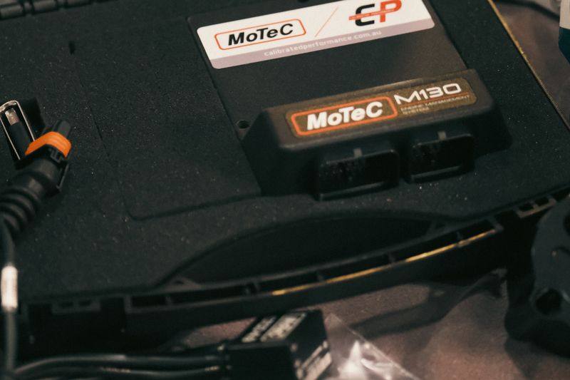 A MoTeC M130 engine control unit in its box, laid out on a dark cloth alongside the wiring loom and sensors.