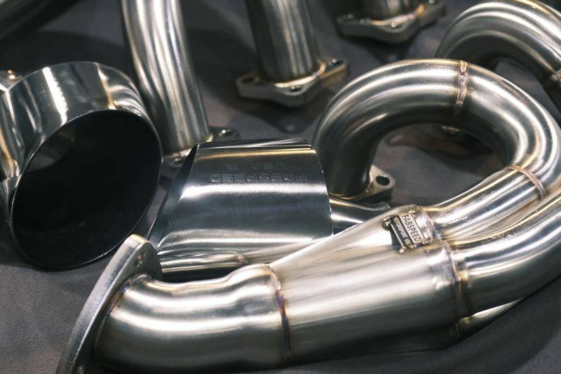 Polished stainless steel exhaust headers and collectors arranged on a dark cloth.